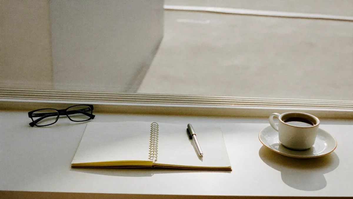 A planning desk with a blank notepad, pen, glasses and coffee