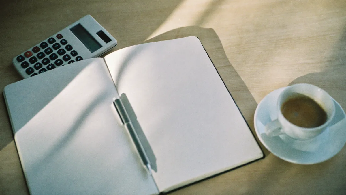 A notebook, pen and calculator on a sunlit desk