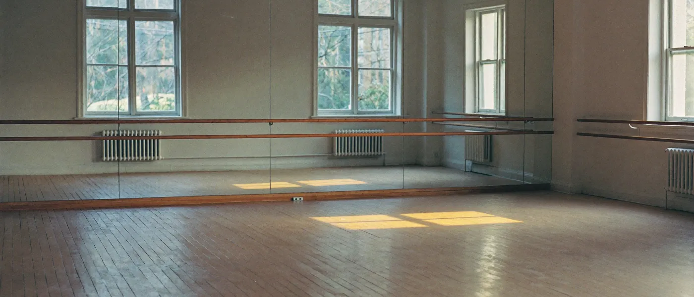 An empty dance studio with a mirrored wall and a ballet barre