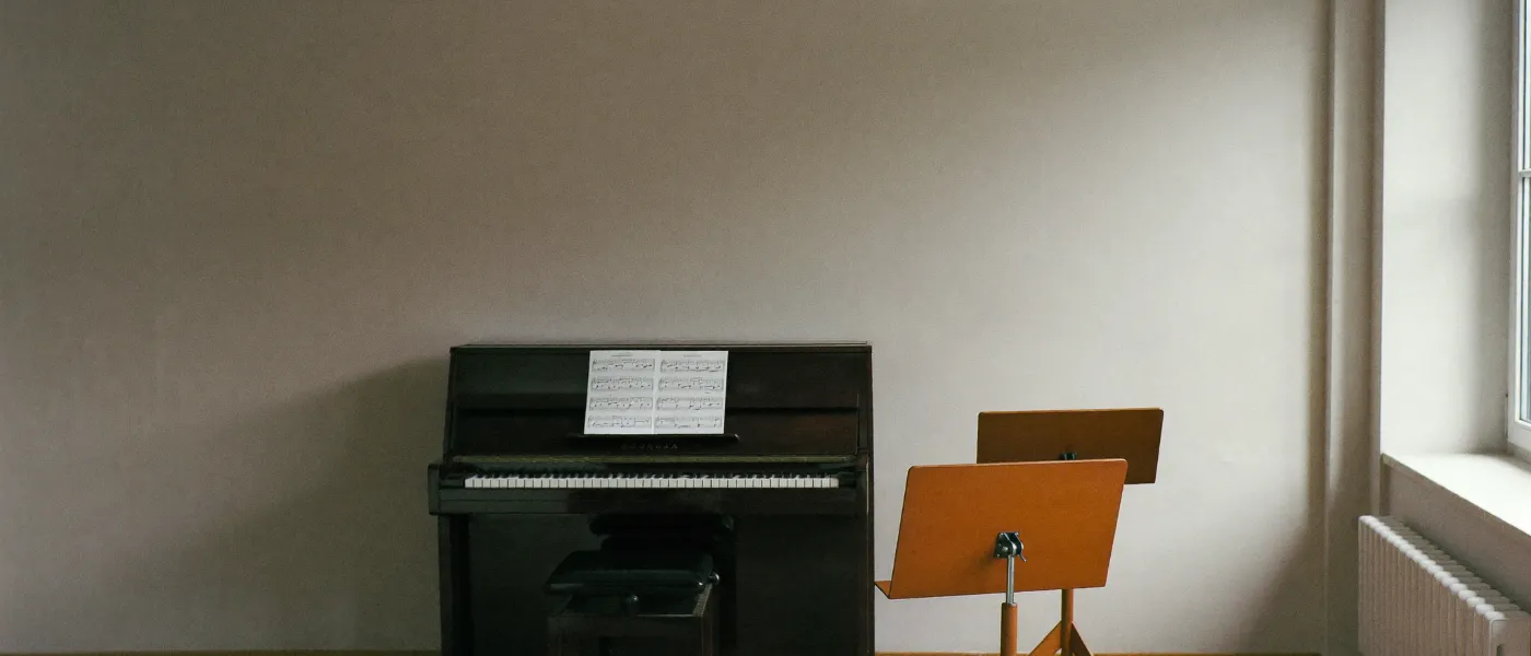 A music school practice room with an upright piano and music stands