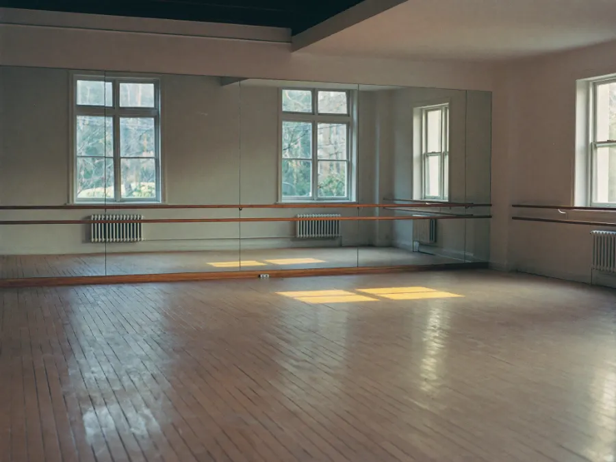 An empty dance studio with a mirrored wall and a ballet barre